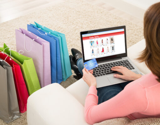 What makes the people tend towards shopping? A girl sitting on sofa and hold the laptop, credit card and shopping near to sofa